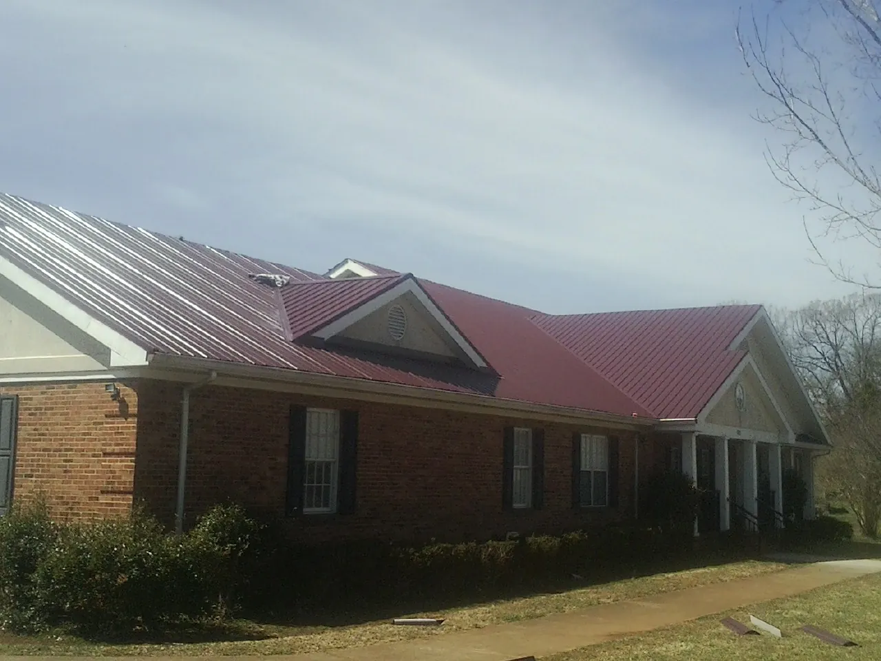 Red metal roof with gabled entries on a long brick building, from a Hail Damage Roof Repair job in Orange City