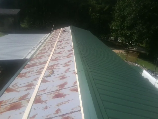 Old rusted panels beside newly installed green metal roofing — Wind Damage Roof Repair by Roofing Brothers in Orange City