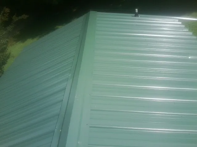 New green metal panels meeting at the ridge of a roof — Flat Roof Repair work by our crew in Orange City