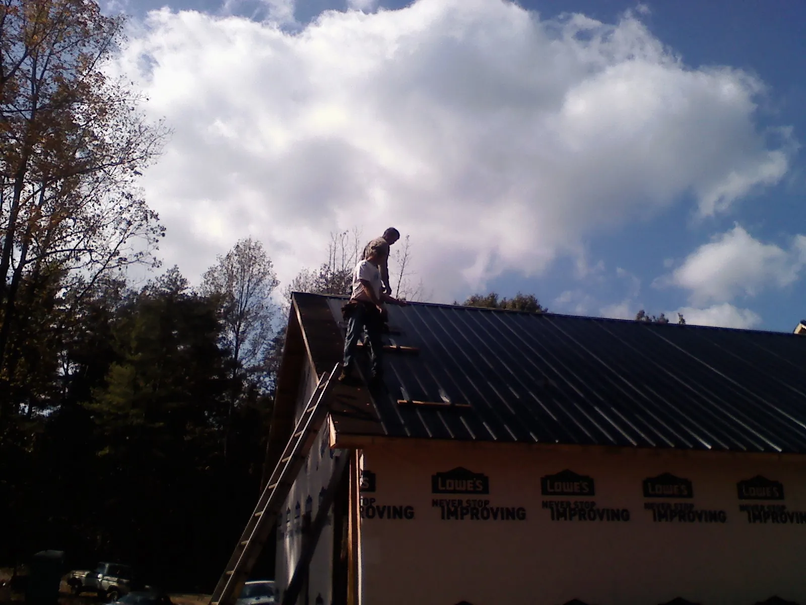 Roofer fastening dark metal panels high against a cloudy sky, from a Roof Inspection job in Orange City