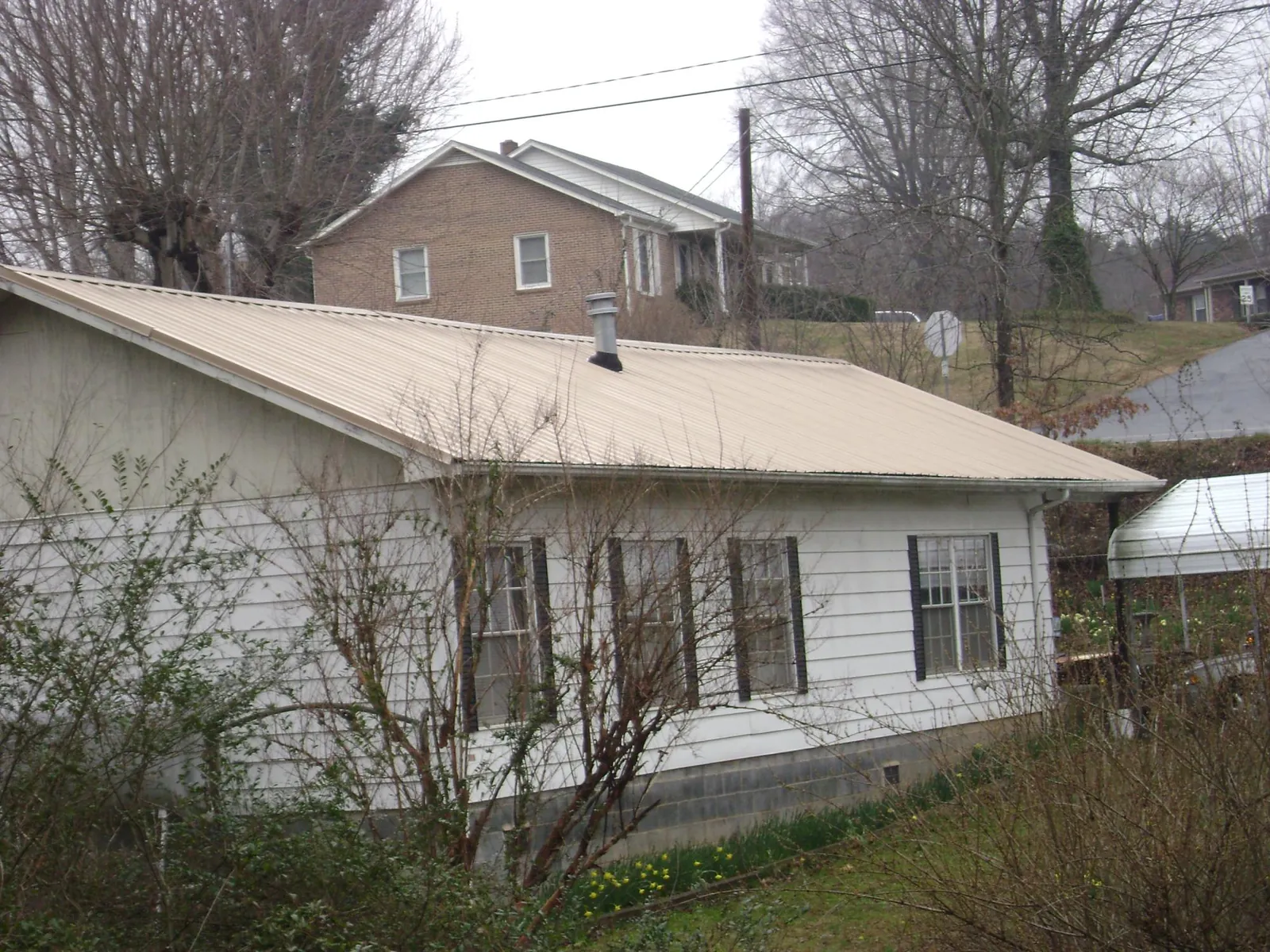 Tan metal roof on a white sided house set into a hillside — Commercial Roofing by Roofing Brothers in Orange City